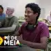 Estudante com fones de ouvido no pescoço sorrindo em sala de aula com outros alunos ao fundo e logo Pé-de-Meia.