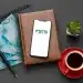 Celular com aplicativo FGTS sobre agenda de couro ao lado de notas de cem reais caneta e xícara de café.