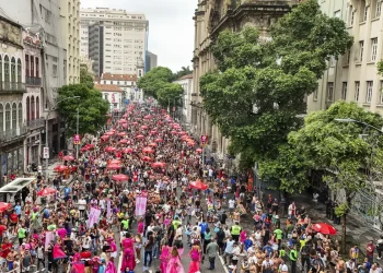 Multidão celebra Carnaval com blocos e guarda-sóis vermelhos nas ruas do Centro do Rio de Janeiro.