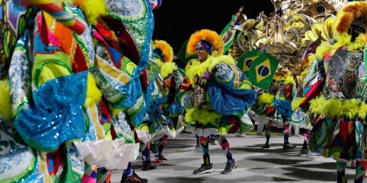 Integrantes de escola de samba desfilam no Carnaval 2026 com fantasias coloridas e bandeiras do Brasil.