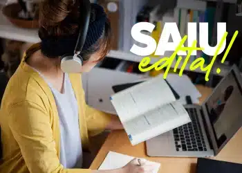 Mulher estudando em casa para concurso público com fones de ouvido. Edital com mais de 700 vagas e salários até R$ 5,9 mil.