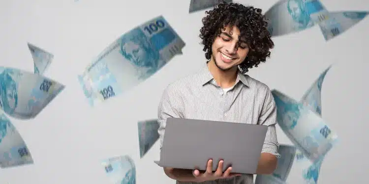 Homem sorrindo enquanto consulta um laptop, com notas de dinheiro ao fundo, representando a consulta de valores financeiros.