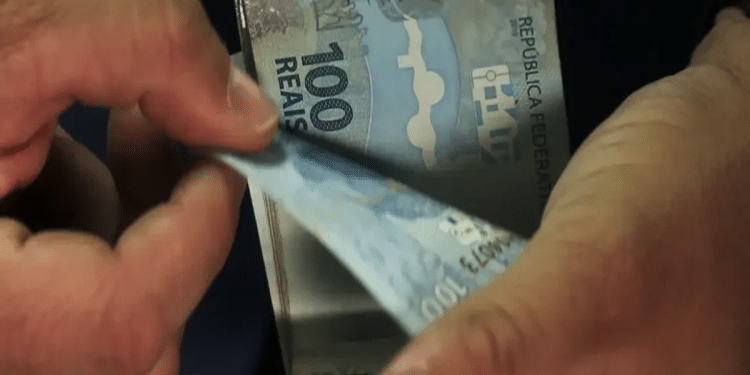 Duas mãos segurando várias notas de cinquenta reais do Banco Central do Brasil.