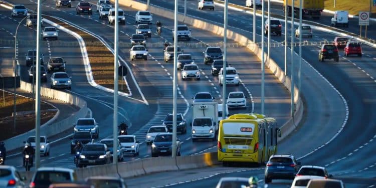Vista aérea de uma rodovia movimentada com várias faixas repletas de carros, ônibus e motocicletas circulando sob a luz do entardecer.