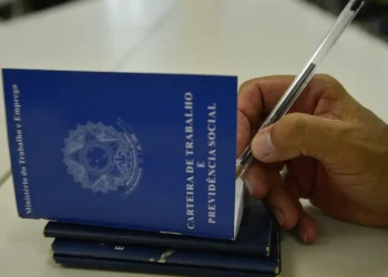 Carteira de Trabalho sendo preenchida com caneta, representando o registro de um trabalhador, em contexto de mudanças na escala de trabalho 6×1 no Brasil.