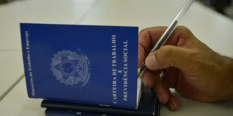 Carteira de Trabalho sendo preenchida com caneta, representando o registro de um trabalhador, em contexto de mudanças na escala de trabalho 6×1 no Brasil.
