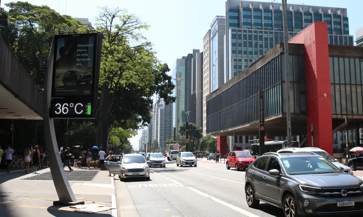 guia como obter desconto maximo ipva 2026 Fotografia da Avenida Paulista em um dia ensolarado, mostrando um relógio de rua marcando 36°C e o trânsito de carros em frente ao prédio do MASP.