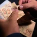Mãos segurando notas de cinquenta reais representando aumento de pagamento do INSS e BPC em janeiro de 2026.