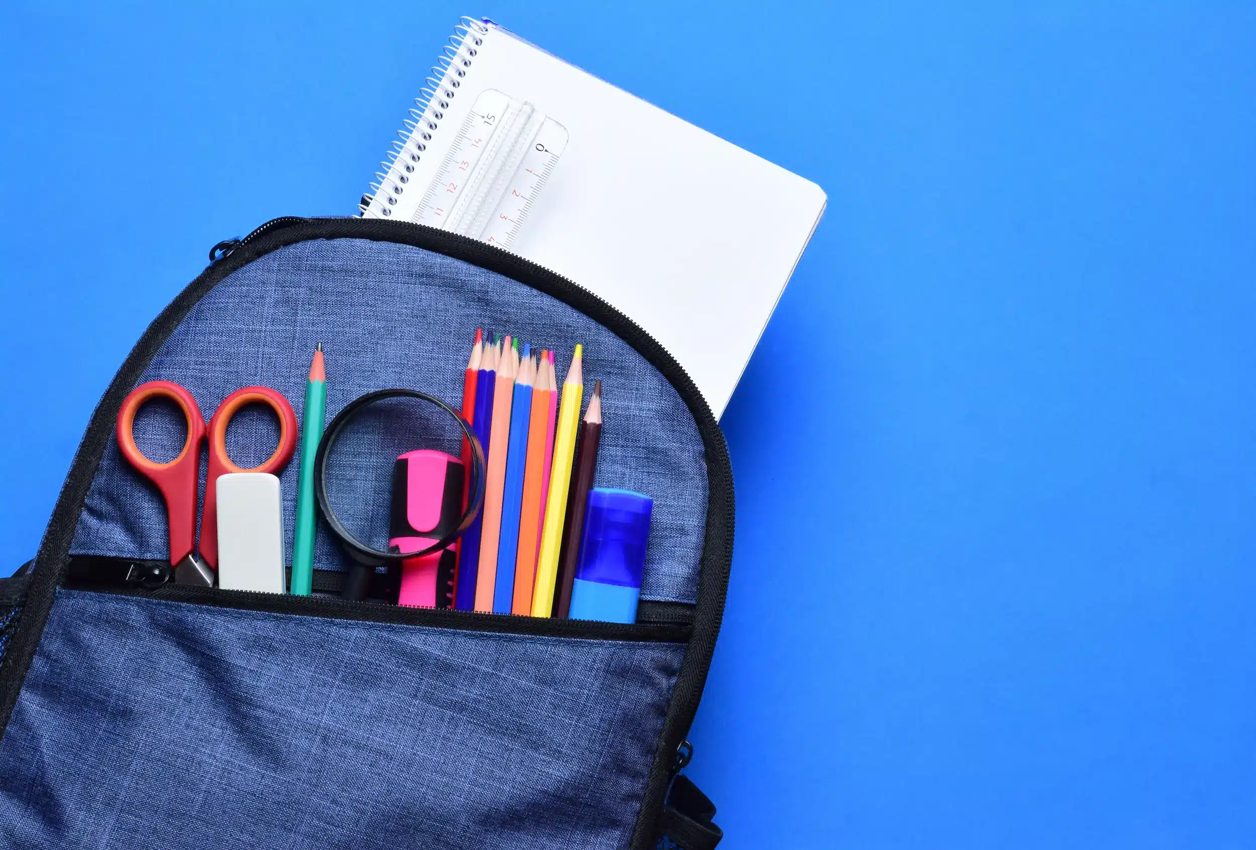 Mochila escolar com lápis de cor, tesoura, caderno e outros itens.