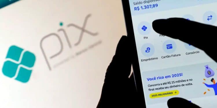 Foto em close de uma pessoa utilizando um smartphone para acessar o aplicativo de um banco, com o logotipo do Pix visível ao fundo em uma tela de computador.