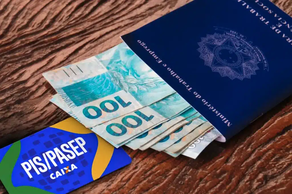 Notas de cem reais ao lado de carteira de trabalho e cartão PIS/PASEP ilustram prazo final para solicitar ressarcimento de valores esquecidos.