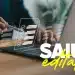 Mãos escrevendo em um laptop com documentos sendo assinados digitalmente, representando abertura de edital.