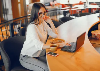 Profissional trabalhando remotamente em um café, com computador e xícara de café, representando uma profissão que pode pagar mais de R$ 10 mil por mês.