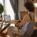 Mulher trabalhando de casa com um cachorro no colo, usando um laptop enquanto organiza suas tarefas em um ambiente aconchegante.