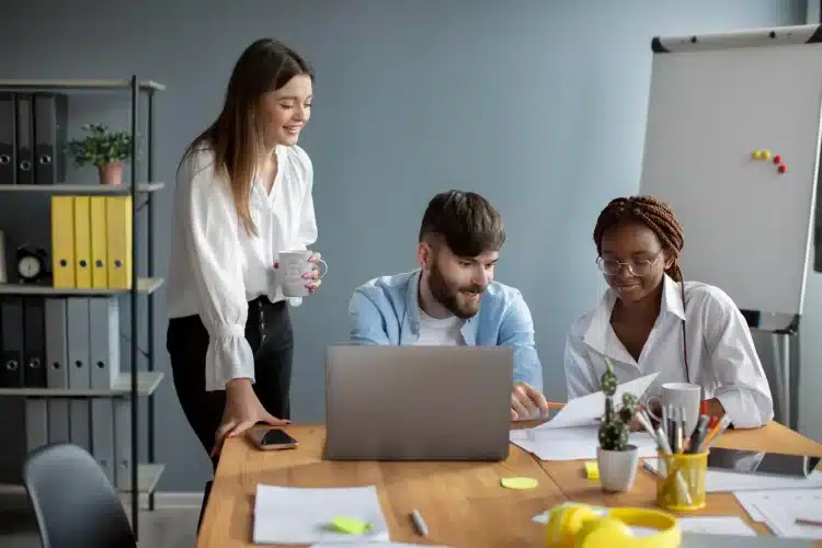 Profissionais discutindo sobre inteligência artificial no ambiente de trabalho, em um escritório moderno com laptop, documentos e café.