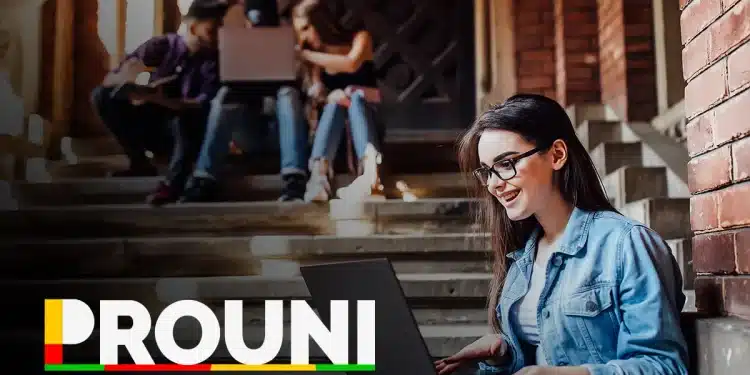 Estudante sorrindo enquanto trabalha no computador em um ambiente acadêmico, com outros estudantes ao fundo, em uma escada de um prédio.