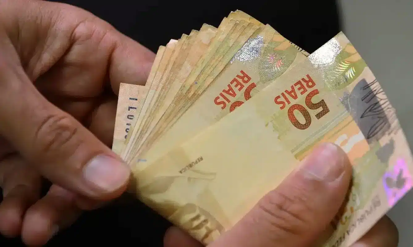 Pessoa segurando cédulas de 50 reais, representando o pagamento dos benefícios do INSS após o reajuste de 2026.