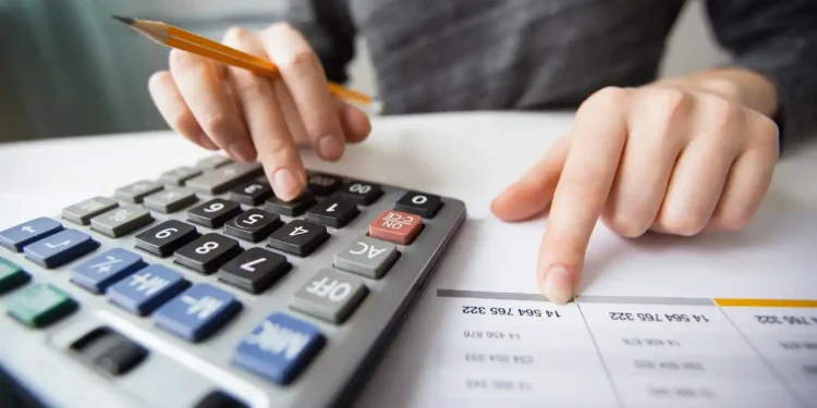 Pessoa utilizando uma calculadora para realizar cálculos financeiros, com uma planilha ao lado.