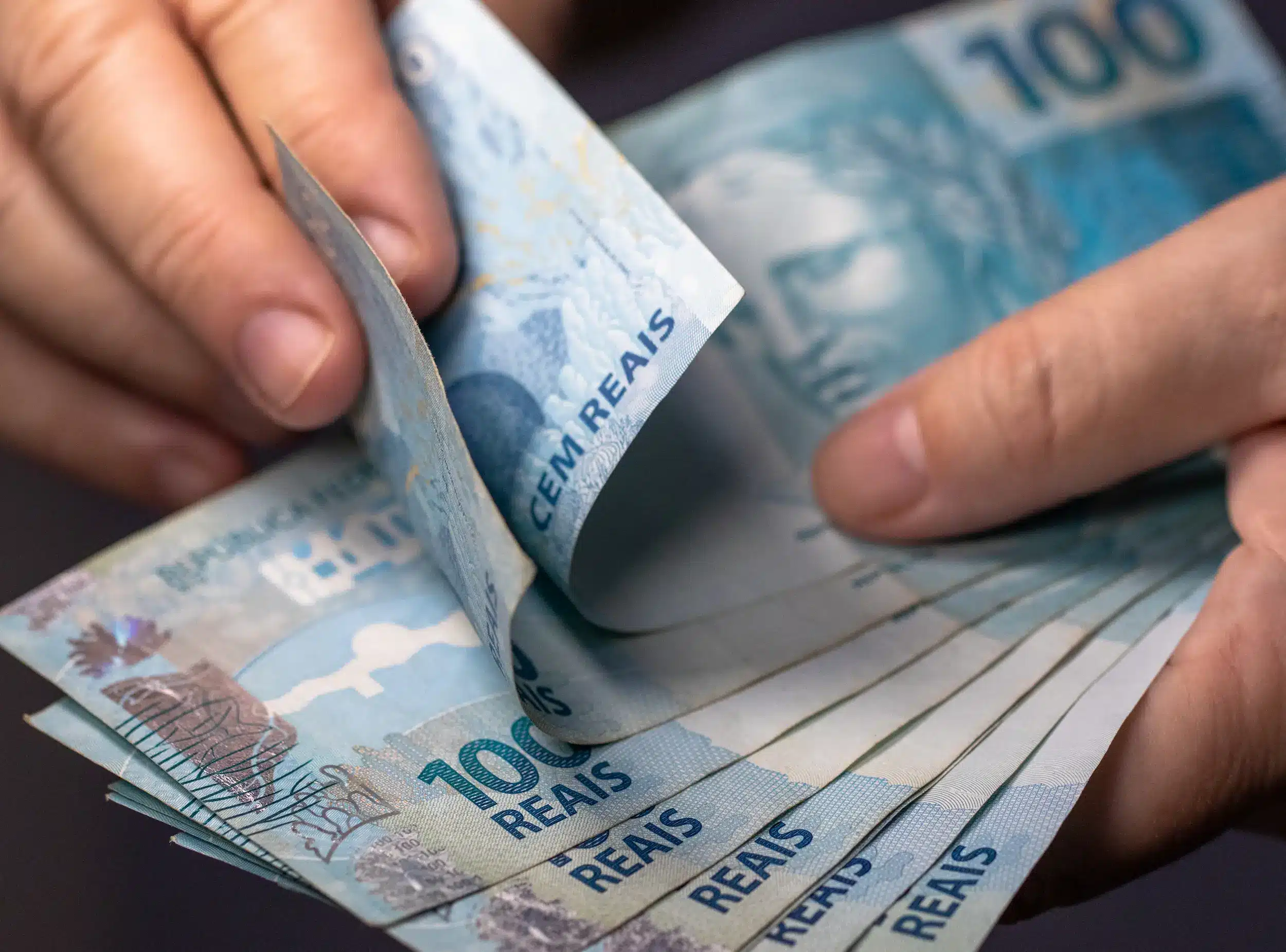 Mãos segurando notas de R$ 100, ilustrando o processo de saque de até R$ 6.220 do FGTS.