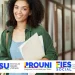 Estudante sorrindo com pastas na mão, representando as opções de ingresso universitário através dos programas Sisu, Prouni e Fies 2026.