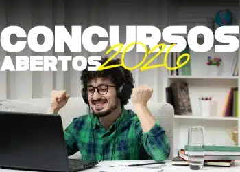 Rapaz sorrindo com fones, punhos erguidos de alegria diante de notebook, material de estudo à mesa.
