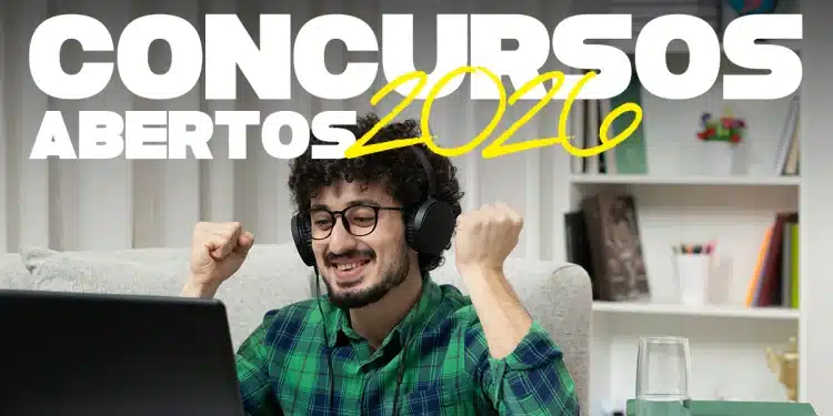 Rapaz sorrindo com fones, punhos erguidos de alegria diante de notebook, material de estudo à mesa.
