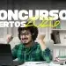 Rapaz sorrindo com fones, punhos erguidos de alegria diante de notebook, material de estudo à mesa.