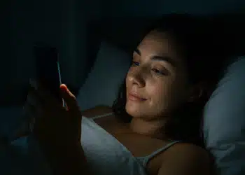 Mulher deitada na cama usando o celular à noite.