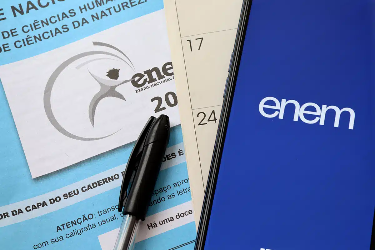 Folha de prova do Enem com caneta ao lado de celular exibindo a Página do Participante.