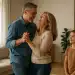 Casal dançando sorridente na sala com uma criança observando.