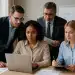 Equipe de quatro pessoas em reunião de trabalho analisando informações em um laptop.