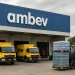 Empilhadeira transportando carga de bebidas enquanto caminhões amarelos aguardam no galpão da Ambev.