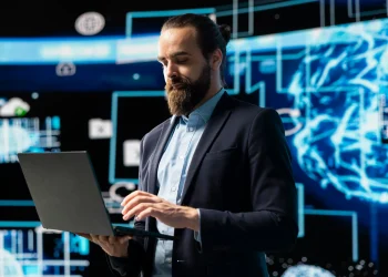 Homem de negócios com laptop em frente a gráficos de dados digitais, representando uma área de tecnologia de alta remuneração.