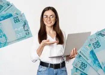 Profissional segurando notebook com notas de R$ 100 ao redor, simbolizando carreiras que alcançam altos salários no mercado CLT.