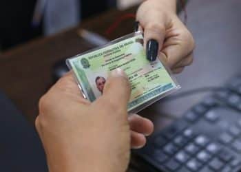 Mãos segurando a nova Carteira de Identidade Nacional com padrão único brasileiro