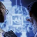 Duas pessoas analisando projeção de dados digitais em tela azul com tablet em mãos