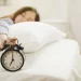 Pessoa deitada na cama apertando o despertador para adiar o alarme pela manhã.