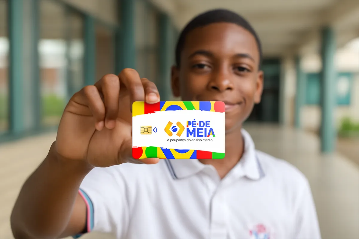 Adolescente segura cartão colorido do Pé-de-Meia com sorriso em ambiente de escola