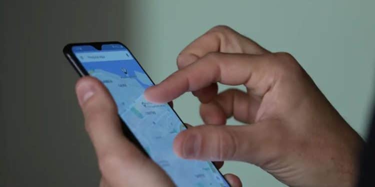Close-up de uma mão segurando um smartphone que exibe a tela inicial do aplicativo Celular Seguro do Governo Federal. Ao fundo, um ambiente urbano levemente desfocado sugere o uso da ferramenta em situações de emergência na rua.