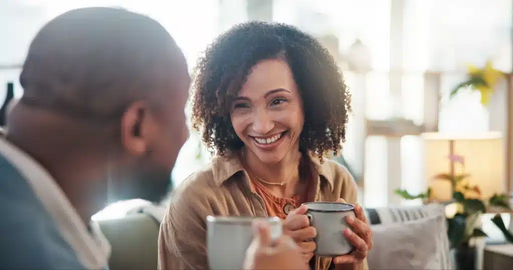 Casal sorrindo e se conectando enquanto tomam café em um ambiente confortável, representando uma boa comunicação.