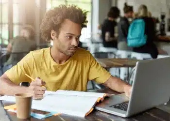 Pessoa estudando com livros e laptop, buscando aprimorar seus estudos para concursos, como os do Cebraspe.