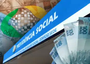 Composição visual com o logotipo da Previdência Social em destaque sobre uma placa azul do INSS, cercada por leques de cédulas de 100 reais, representando o pagamento de benefícios.