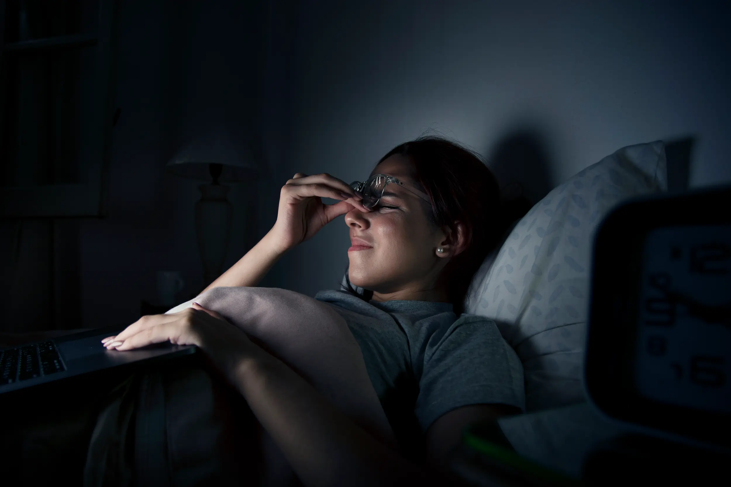 Mulher acordada na cama à noite usando notebook, representando os impactos de dormir tarde na saúde.
