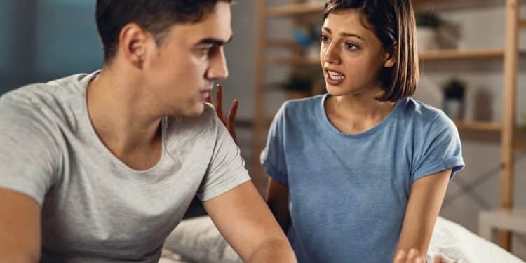 Homem e mulher sentados em um quarto conversam de forma séria, expressando emoções durante um conflito no relacionamento.