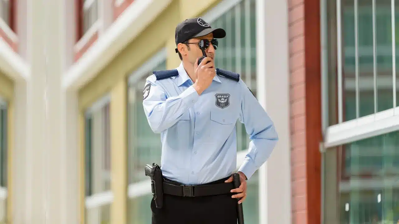 Vigilante de segurança usando rádio de comunicação em frente a prédio.