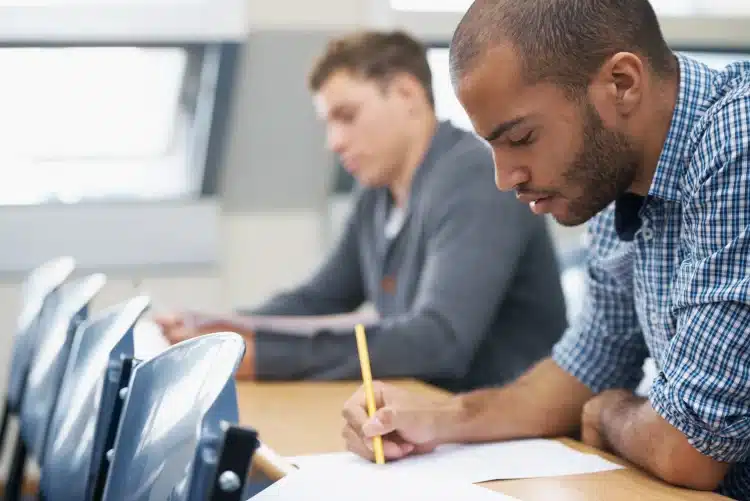 Dois candidatos escrevendo atentamente durante prova em sala iluminada