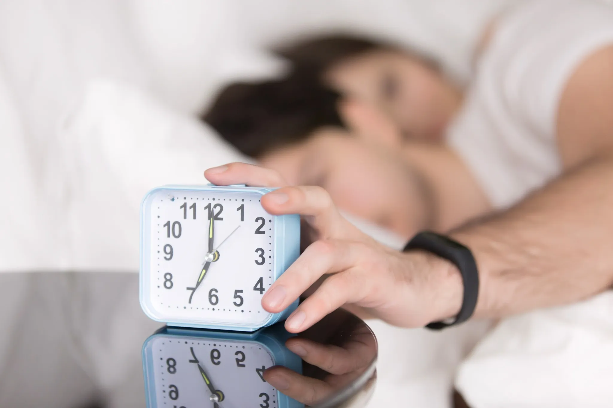 Pessoa desligando despertador pela manhã enquanto permanece deitada na cama.