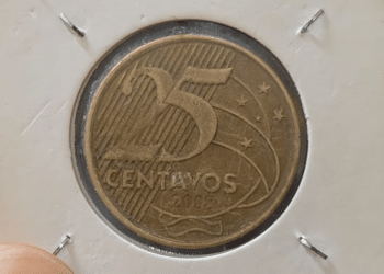 Close-up de uma moeda de 25 centavos de 2008 guardada em um suporte de proteção branco (coin holder), destacando o número 25 e o ano de cunhagem sobre o fundo dourado.