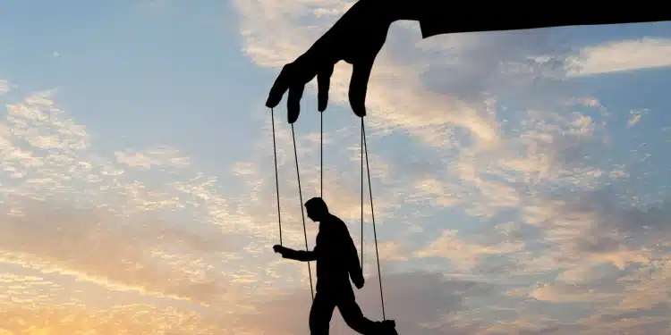 Silhueta de mão gigante controlando homem com fios contra céu ao entardecer
