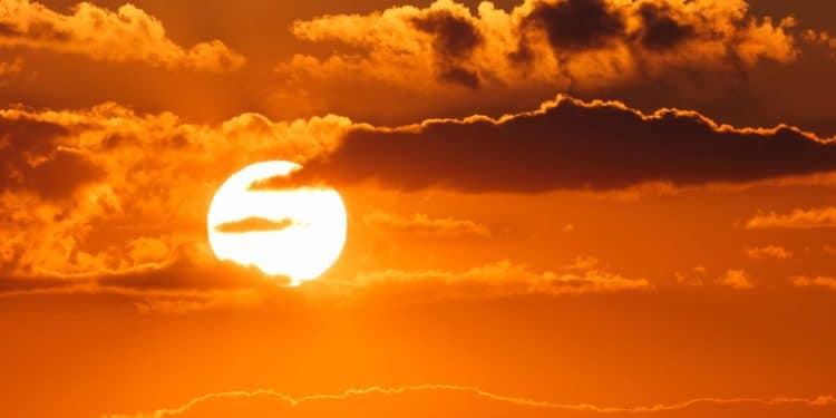 Paisagem de um pôr do sol intenso com o céu em tons de laranja vibrante e nuvens escuras, simbolizando o aquecimento global e as ondas de calor extremo.
